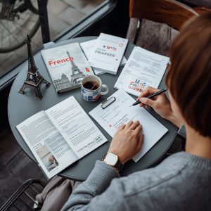 adult learner sitting at a café with several French learning books